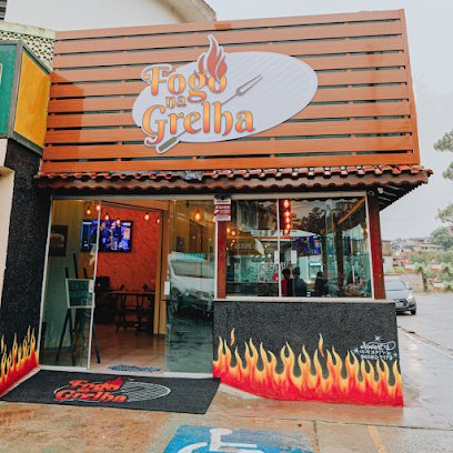 Fachada do restaurante Fogo na Grelha: painel de ripas de madeira terracota com o logotipo em chama, parede preta texturizada com labaredas pintadas e interior iluminado em luz quente
