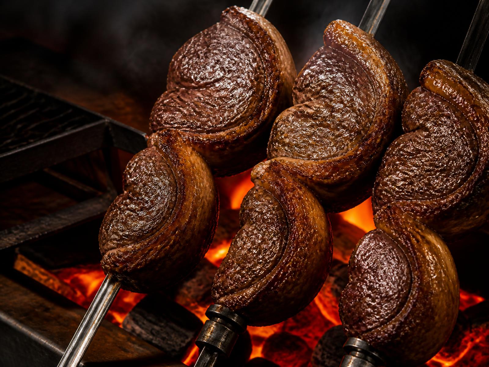 Cortes de carne assando em espetos sobre brasas vermelhas incandescentes na churrasqueira do Fogo na Grelha
